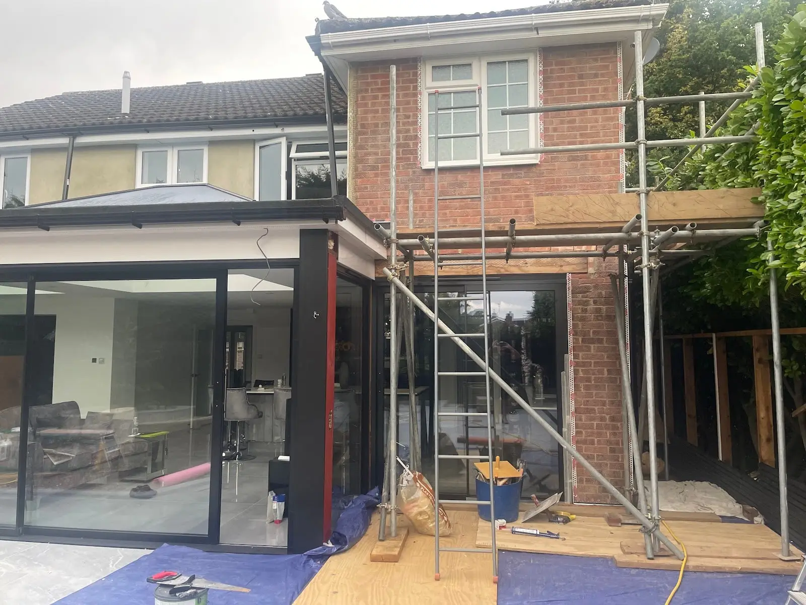 New two-storey side addition in red brick with scaffolding and a ladder, next to a single-storey rear extension
