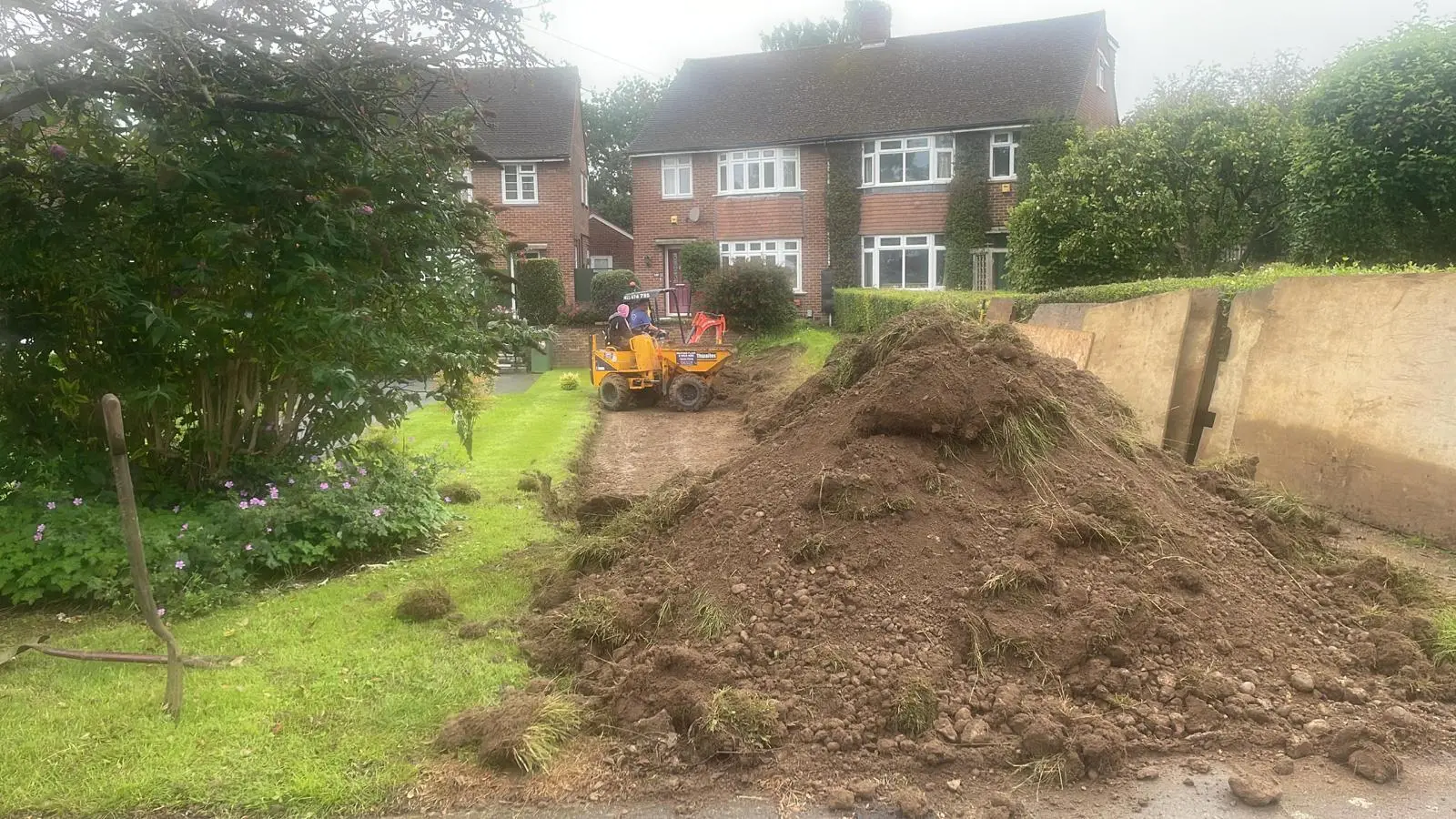 Pile of excavated soil in a front garden, with a dumper ready to take it away