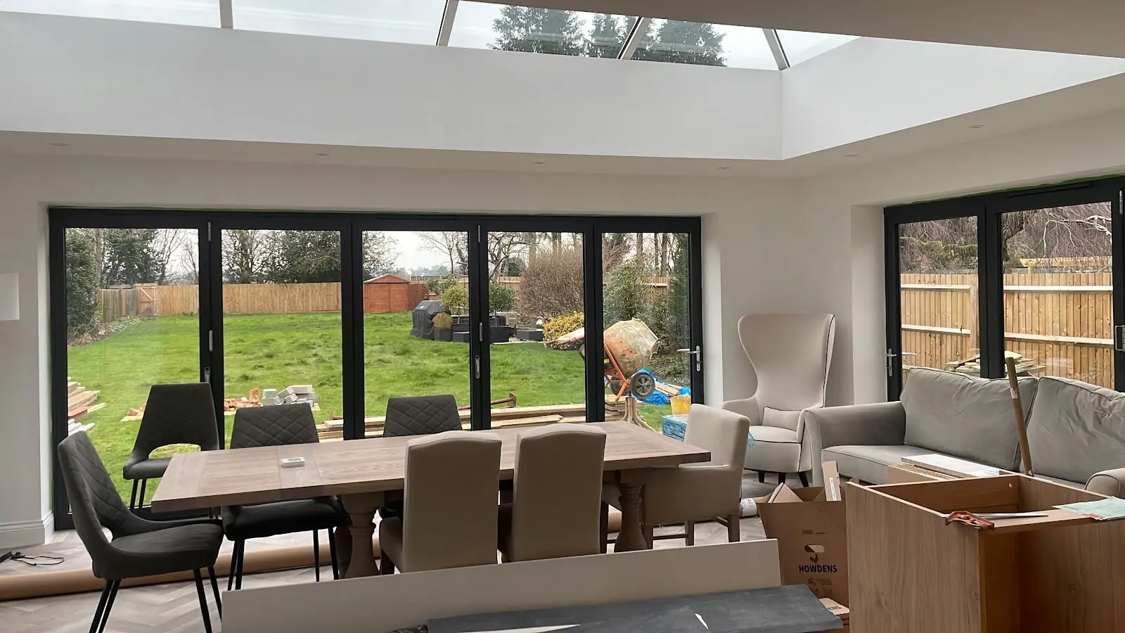 Dining table under a lantern roof light in a kitchen extension, with bi-fold doors open to the lawn