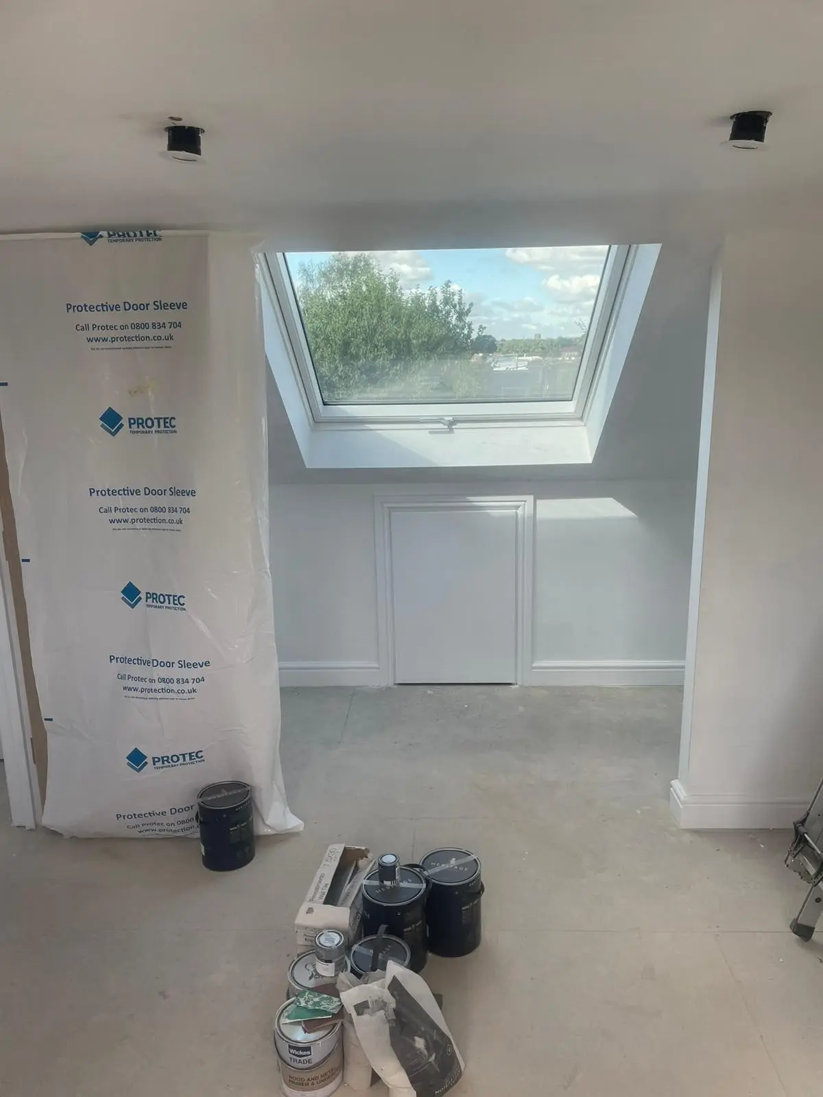 Loft room close to completion, with a roof window, panelled wall and a small door into the eaves