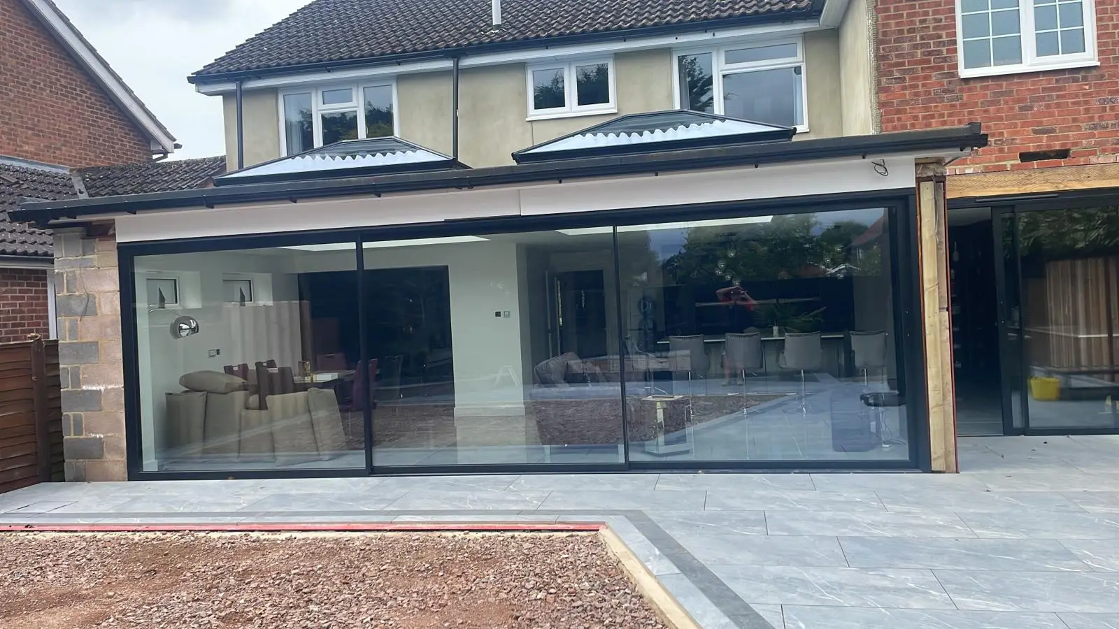 Back of a house with a new single-storey extension: two lantern roof lights and wide sliding glass doors onto a grey porcelain patio