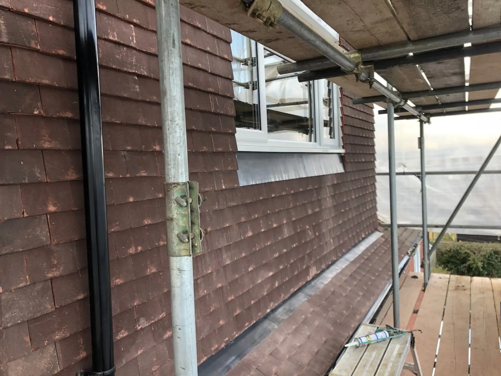 Hung clay tiles on an upper wall next to a new white window, photographed from scaffolding